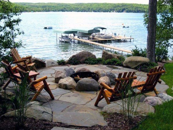 two wooden chairs sitting on top of a stone patio next to a body of water