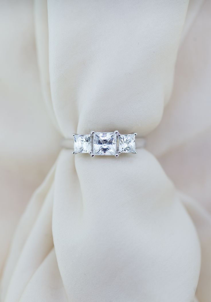 three stone ring sitting on top of a white satin material with the center diamond in between it's sides