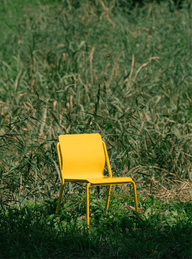 a yellow chair sitting on top of a lush green field next to tall dry grass