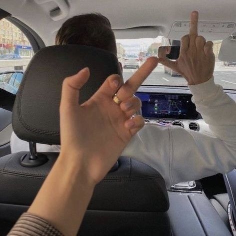 two people sitting in the back seat of a car with their hands up and pointing at something