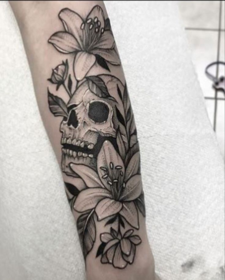 a skull with flowers on it's arm is shown in black and grey ink