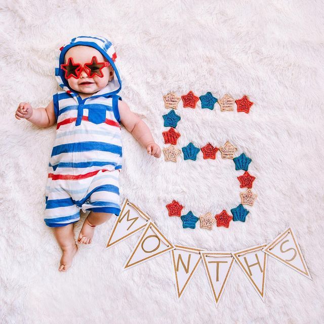 a baby wearing sunglasses laying on top of a white rug next to a letter e