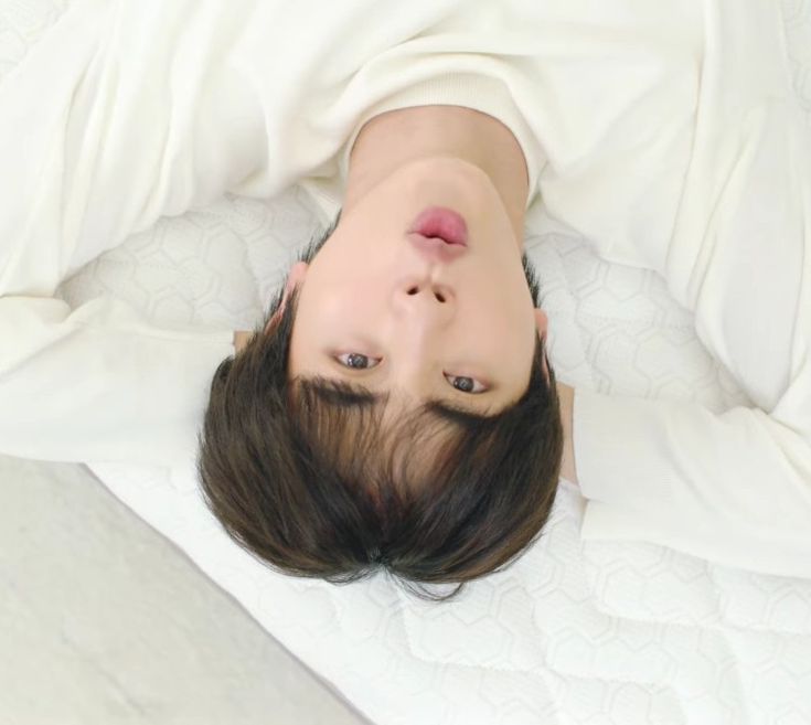 a woman laying on top of a bed under a white blanket with her eyes closed