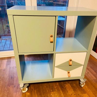 a green and white cabinet sitting on top of a hard wood floor next to a window