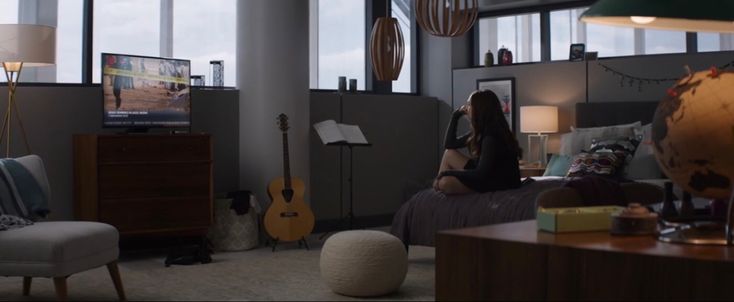 a woman sitting on a bed in a living room with lots of windows and furniture