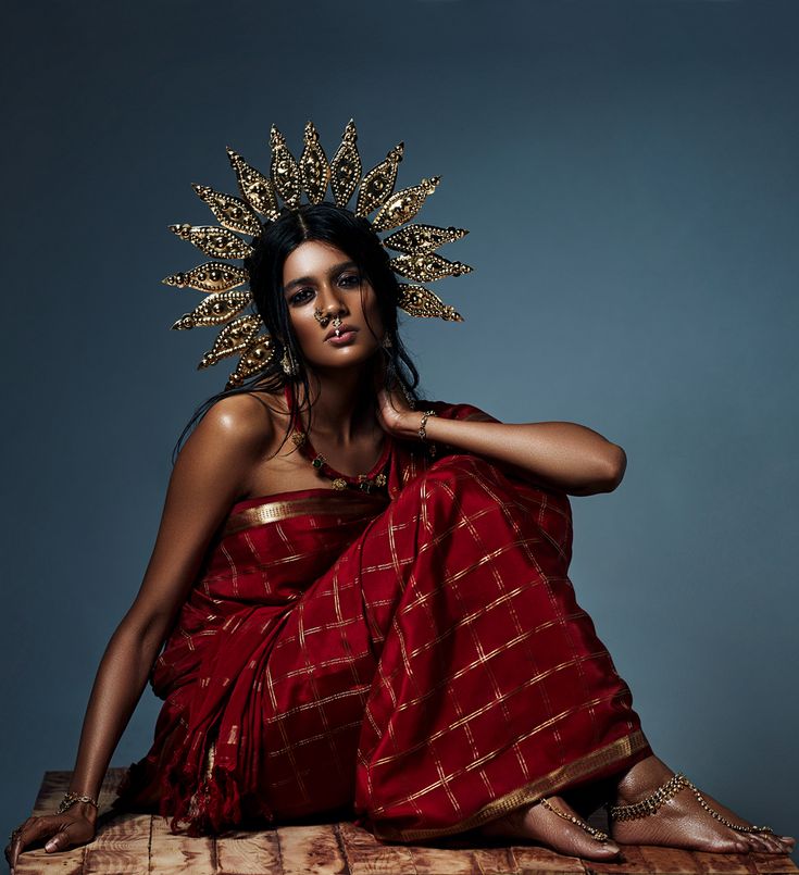 a woman in a red sari sitting on the floor wearing a gold head piece