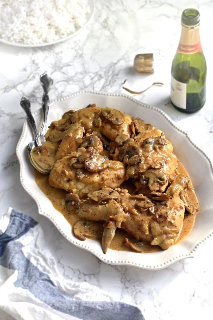 a white plate topped with chicken covered in gravy next to a bottle of wine