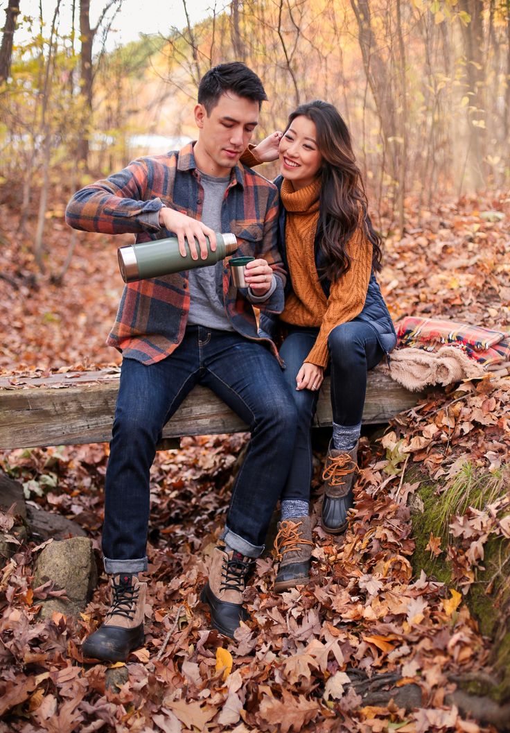 a man and woman sitting on a bench in the woods with autumn leaves around them