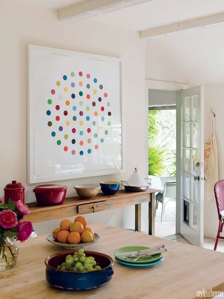 a table with bowls of fruit on it in front of a painting hanging above the dining room table