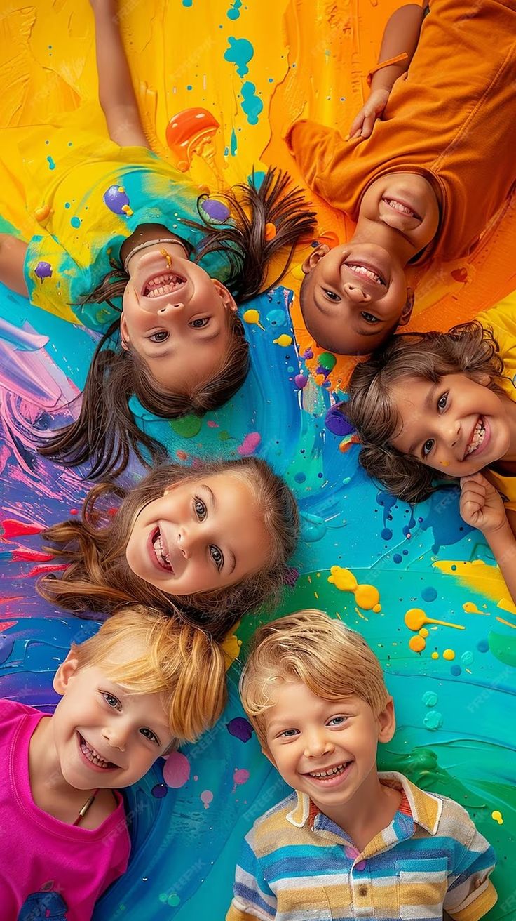 four children laying on the ground with paint all over their bodies and arms, looking up at the camera