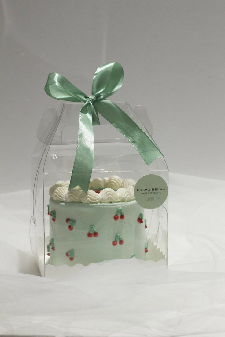 a cake in a clear box with a green ribbon on it's top and white frosting around the edges