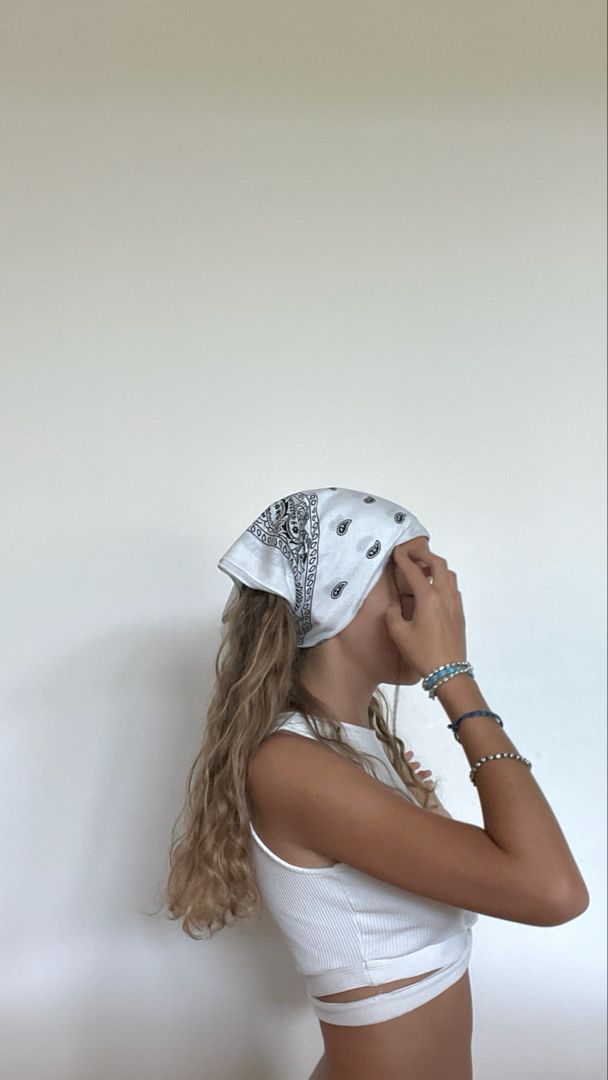 a woman wearing a bandana standing in front of a white wall