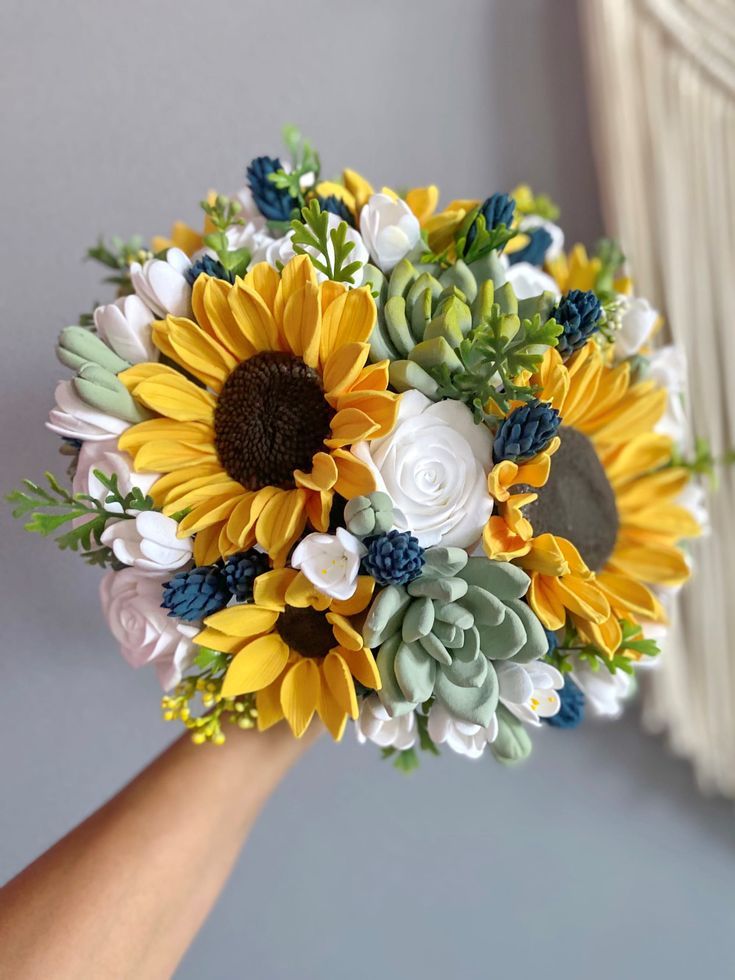 a bridal bouquet with sunflowers and succulents is held by a woman's hand