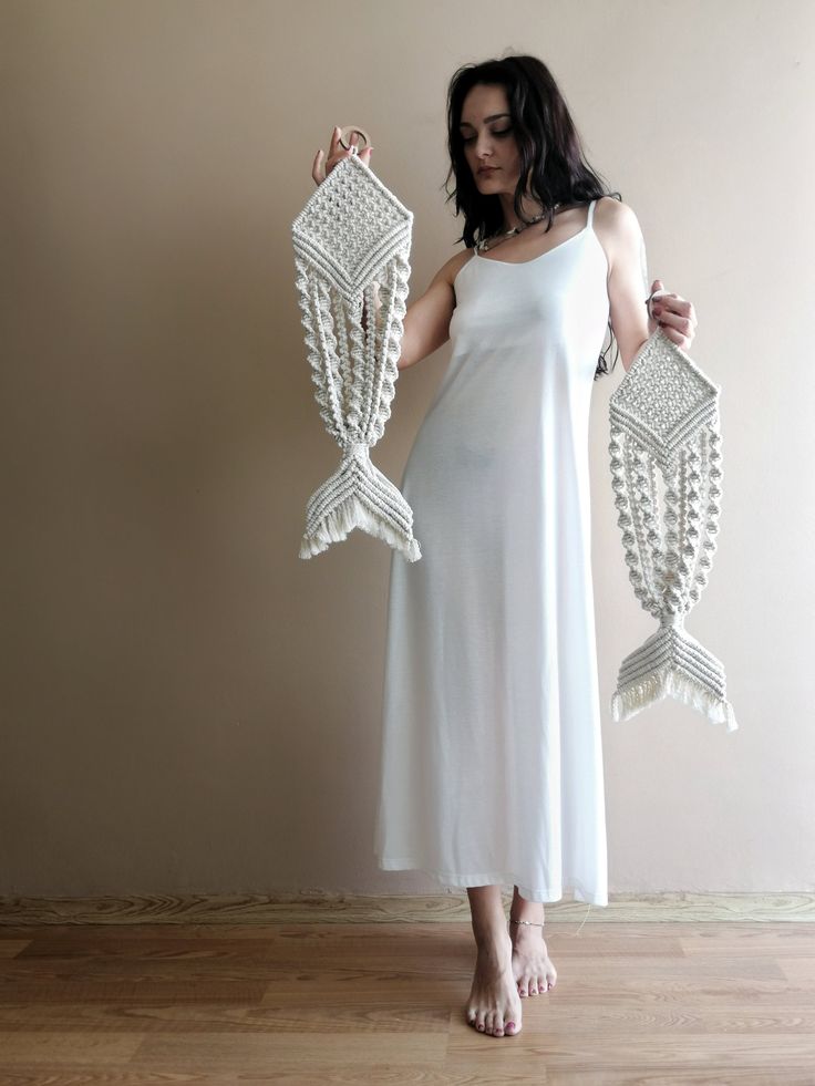 a woman in a white dress is holding two crocheted fish