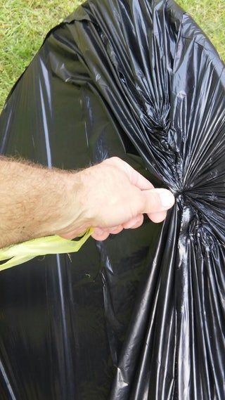 a person holding an umbrella over a black trash bag