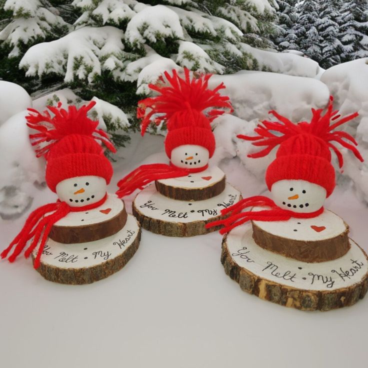 three snowmen with red hats and scarfs are sitting on logs in the snow