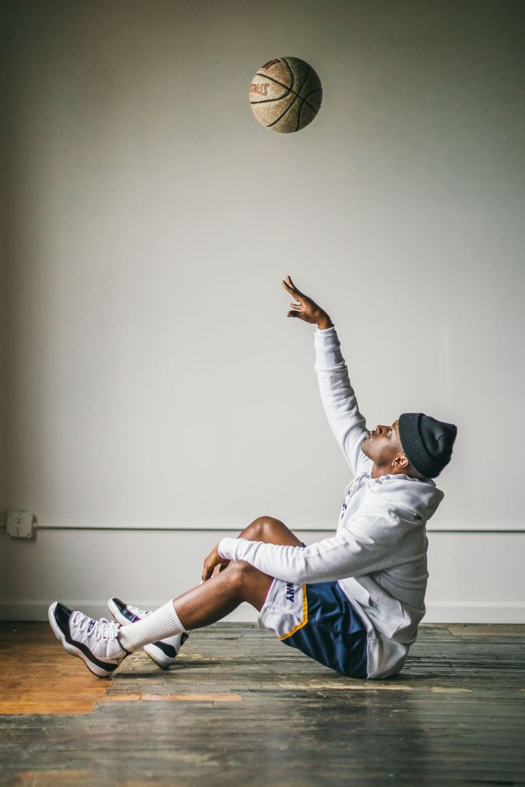 a man is sitting on the floor playing with a basketball and jumping up to catch it