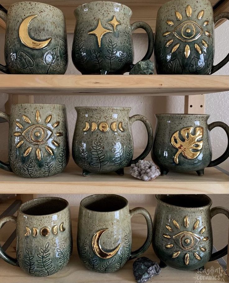 coffee mugs are sitting on shelves with gold designs and moon symbols painted on them