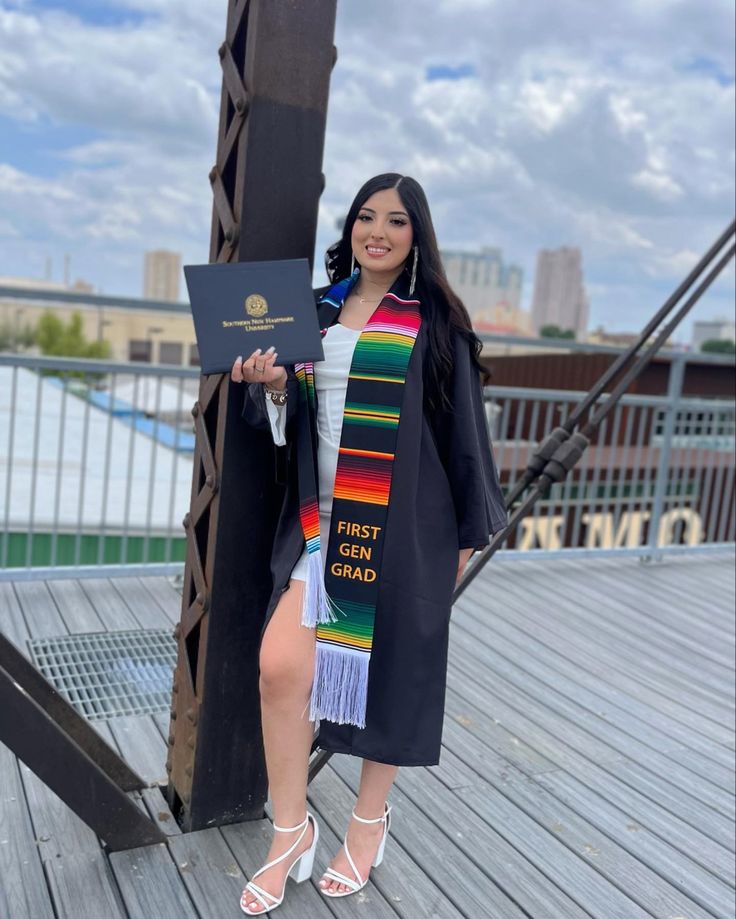 a woman standing on top of a wooden deck holding a book and wearing a graduation gown