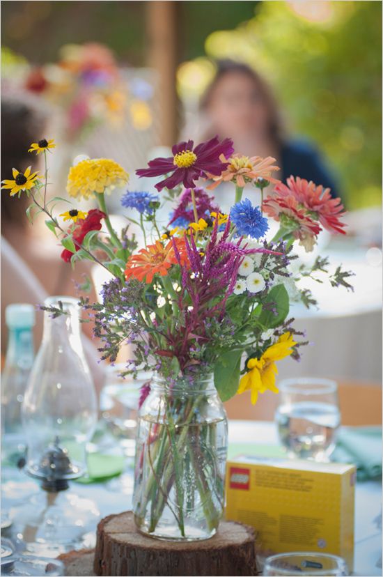 a vase filled with lots of colorful flowers on top of a wooden table next to glasses