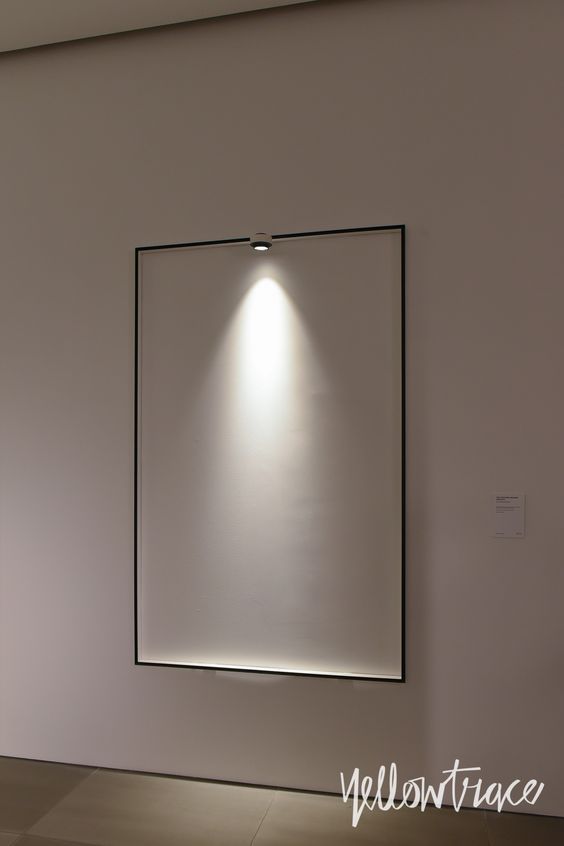 an empty room with a white light on the wall and a black frame hanging from the ceiling