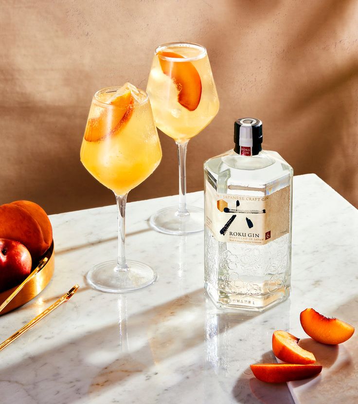 two glasses filled with drinks sitting on top of a table next to apples and orange peels