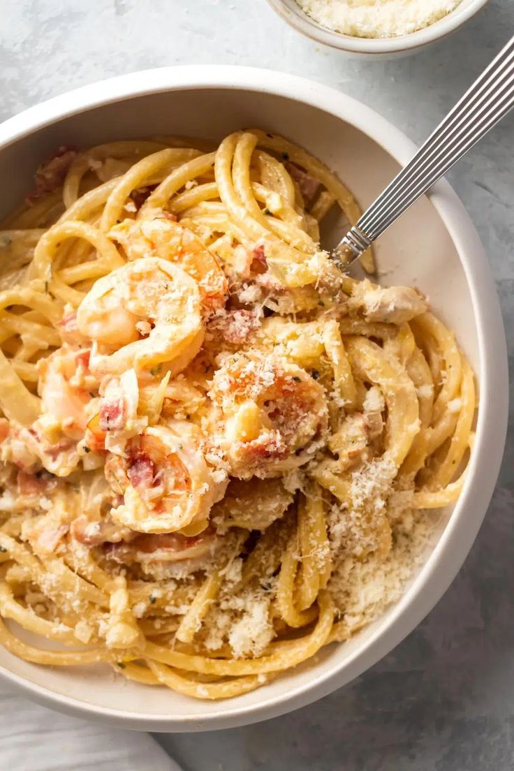 a bowl of pasta with shrimp and parmesan cheese on the side next to a fork