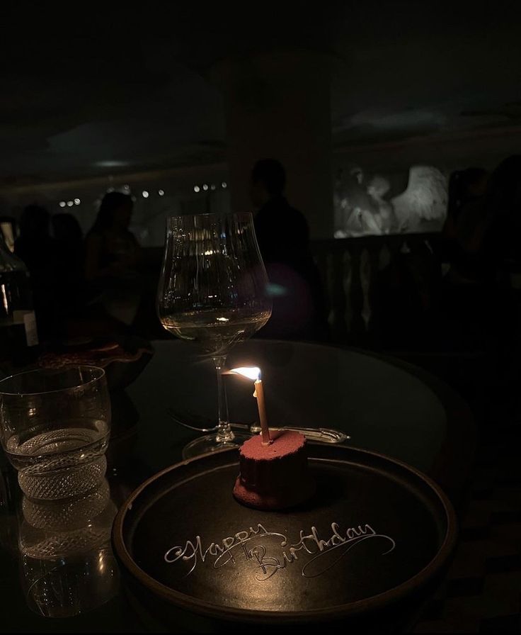 a birthday cake with a candle on it sitting on a table next to two glasses