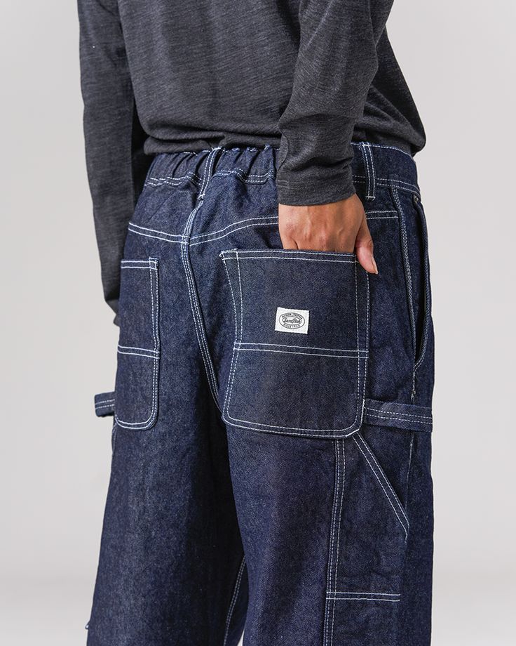 The Recycled Cotton Denim Wide Pants are heavy-weight denim utility pants. The pants feature slanted pockets at the waist, open-top pockets on the back, tool pockets and loops at the thigh on both sides, elastic shirring at the waist, and belt loops. The material is a 12.6oz recycled denim with reinforced stitching. Dark Wash Recycled Denim Cargo Jeans With Belt Loops, Utility Work Pants With Hip Pockets, Dark Wash Recycled Denim Jeans With Cargo Pockets, Urban Rigid Denim Jeans With Hip Pockets, Wide Leg Recycled Denim Cargo Jeans With Patch Pockets, Dark Wash Cargo Jeans With Patch Pockets, Rigid Denim Cargo Jeans With Belt Loops For Streetwear, Streetwear Rigid Denim Cargo Jeans With Belt Loops, Urban Denim Blue Cargo Pants With Belt Loops