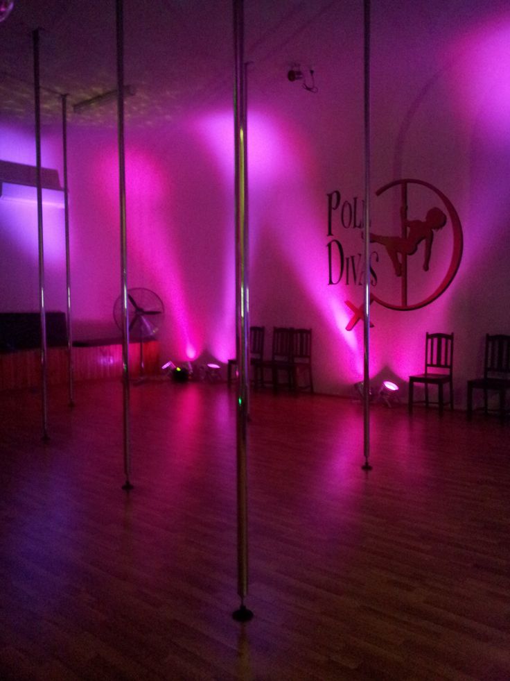 an empty dance floor with pink lights and chairs in the background at pole dancing studio