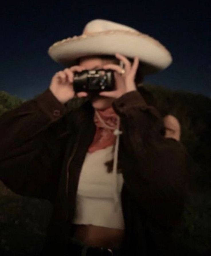 a woman wearing a white hat and holding a camera up to her face while looking into the distance