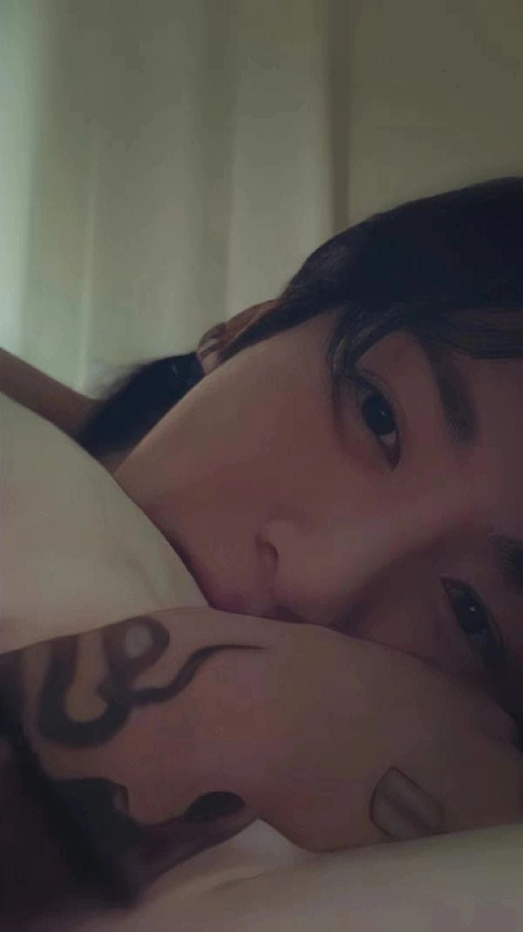 a woman laying in bed with her arm tattoo on top of her head and under the covers