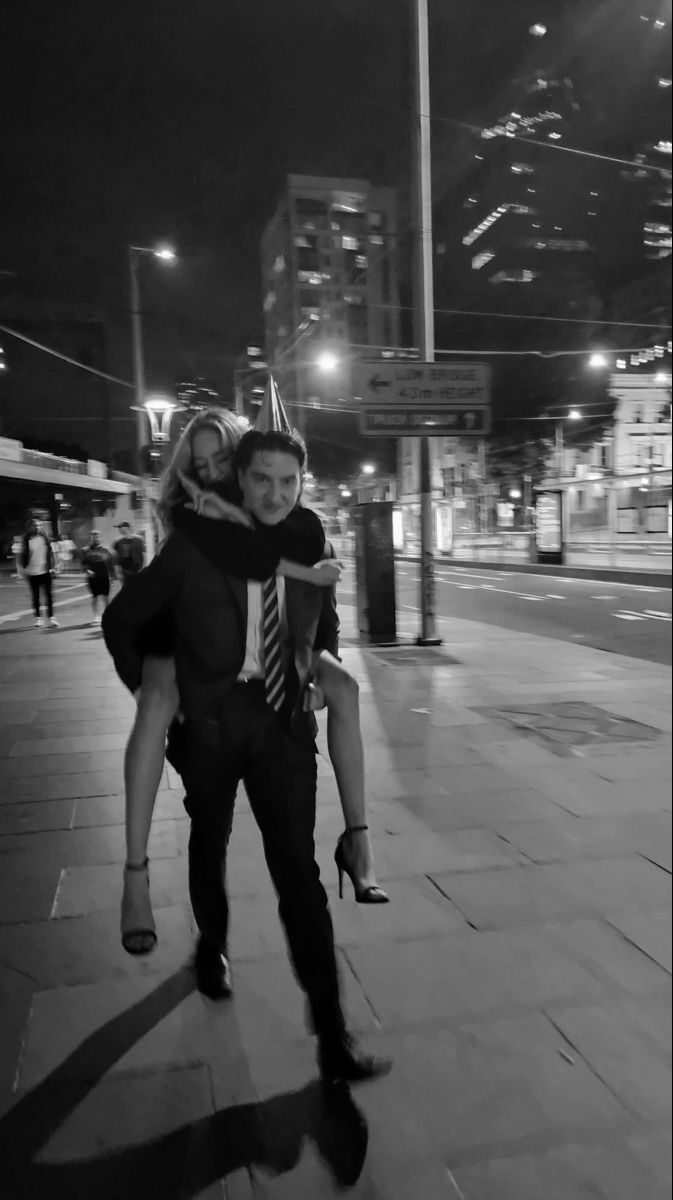 a man carrying a woman on his back down the street at night in black and white