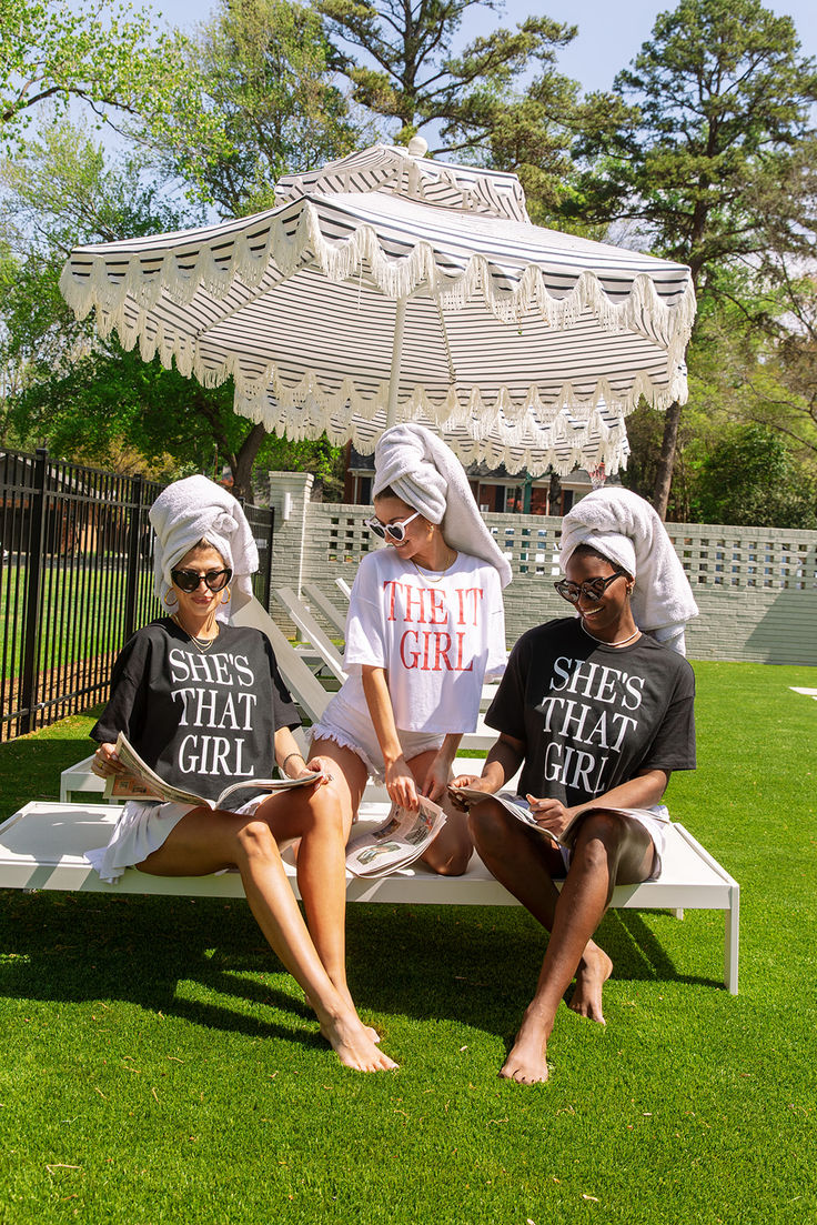 three women sitting on a bench in front of a gazebo wearing matching t - shirts