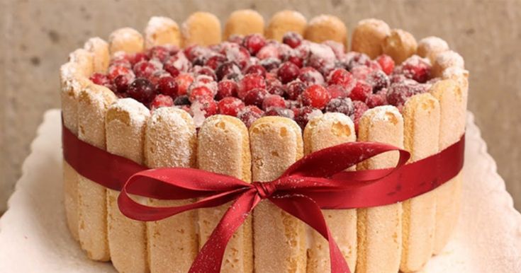 a cake decorated with raspberries and almonds on a white platter, tied with a red ribbon