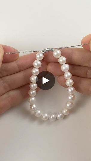 two hands holding white pearls with a video playing on the bead cord in front of them