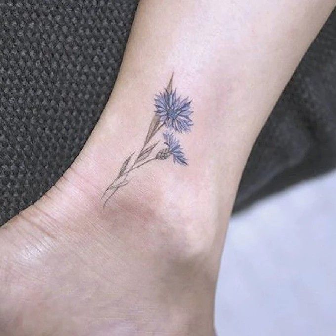 a small blue flower on the ankle tattoo is shown in front of a woman's foot