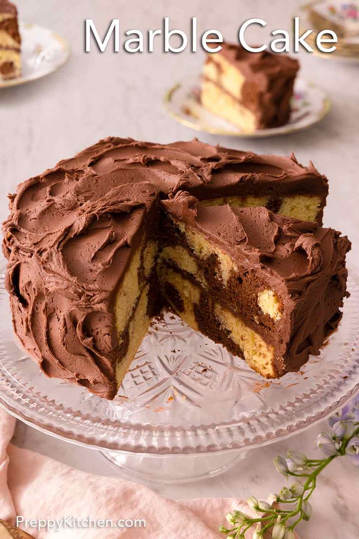 a chocolate cake with one slice missing from it on a glass platter next to other plates