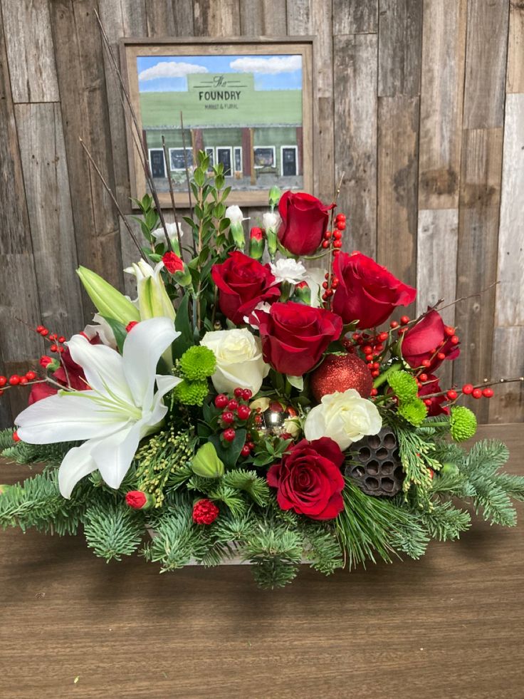 a bouquet of red roses, white lilies and greenery in a wooden box