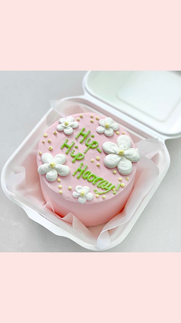 a pink cake with white flowers on it in a plastic container