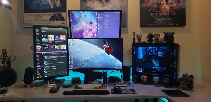 two computer monitors sitting on top of a desk in front of posters and other items