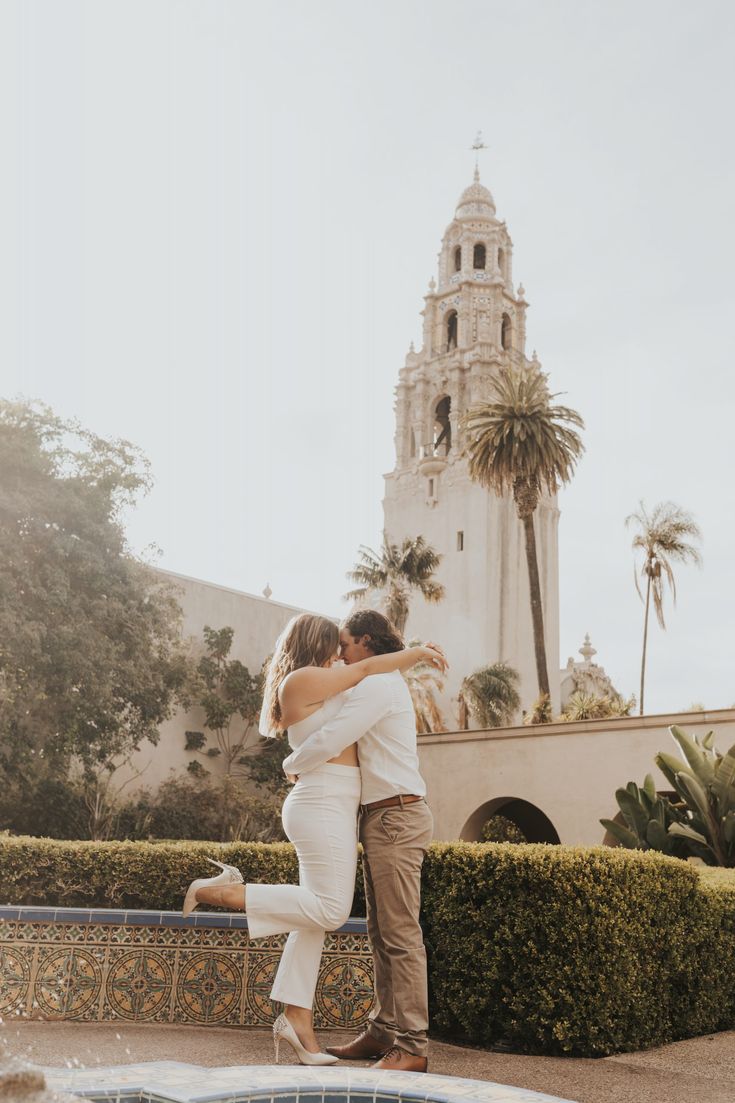 a man and woman embracing in front of a fountain with a church in the background