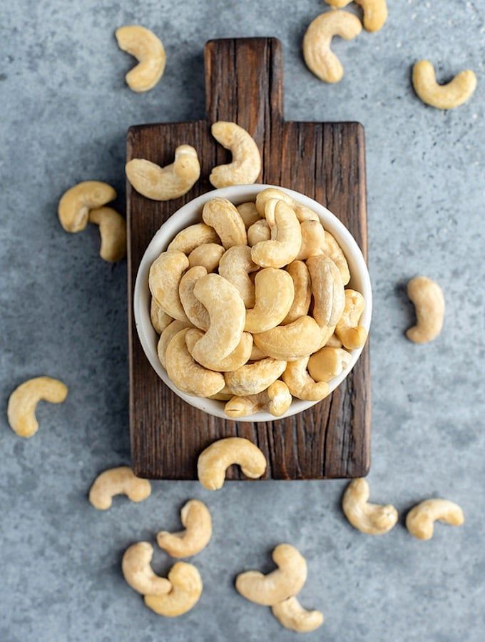 a bowl filled with cashews sitting on top of a wooden cutting board next to some cashews