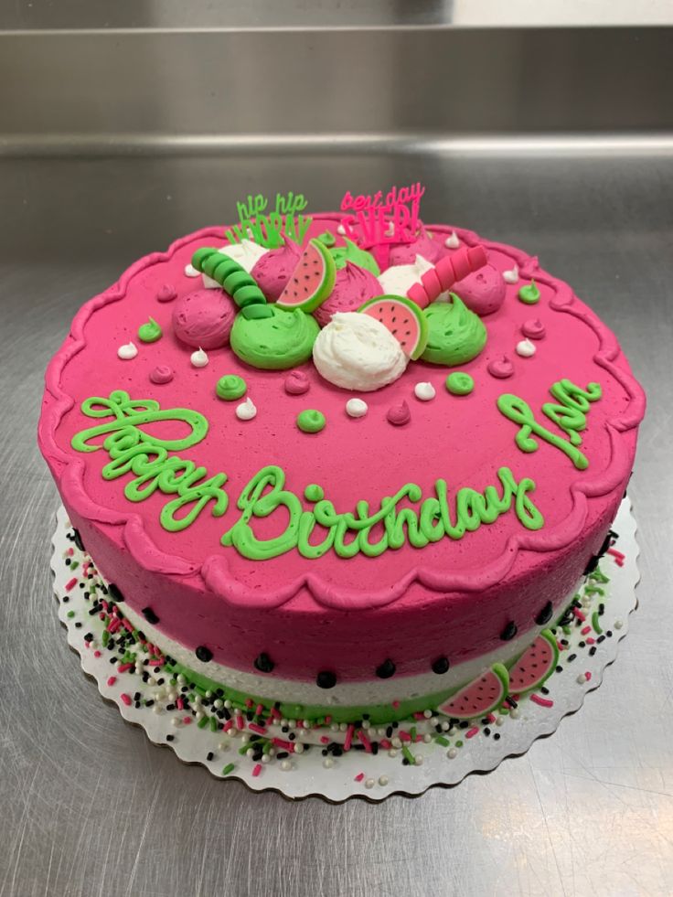 a pink birthday cake with green frosting and decorations on it's top, sitting on a silver surface