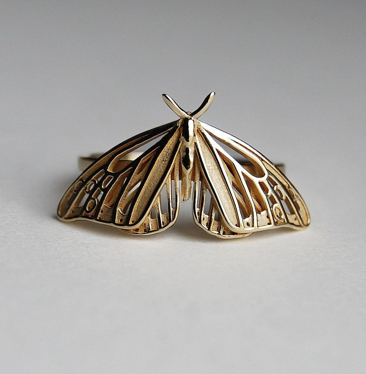 a close up of a butterfly shaped ring on a white surface with one wing extended