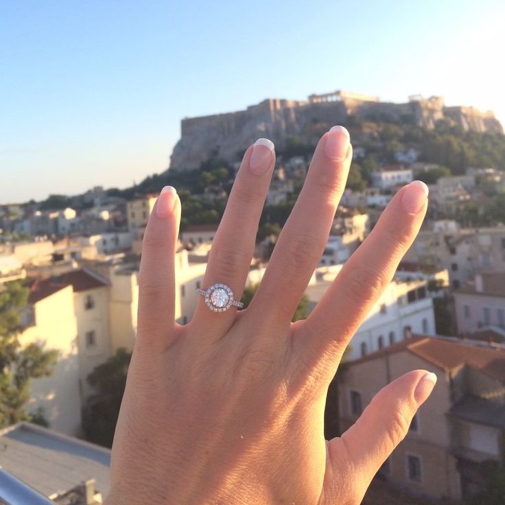 a person's hand with a diamond ring on top of their finger in front of a cityscape