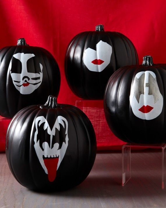 three black pumpkins with white faces and fangs painted on them, sitting in front of a red background