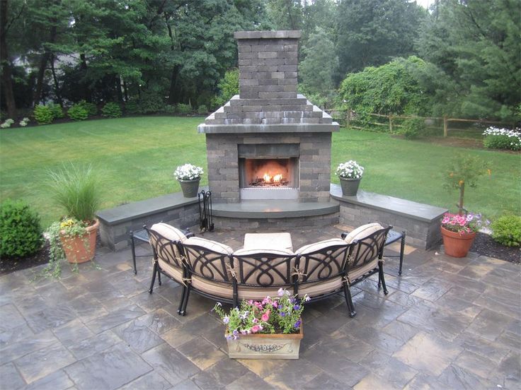 a fire place in the middle of a patio surrounded by flowers and potted plants