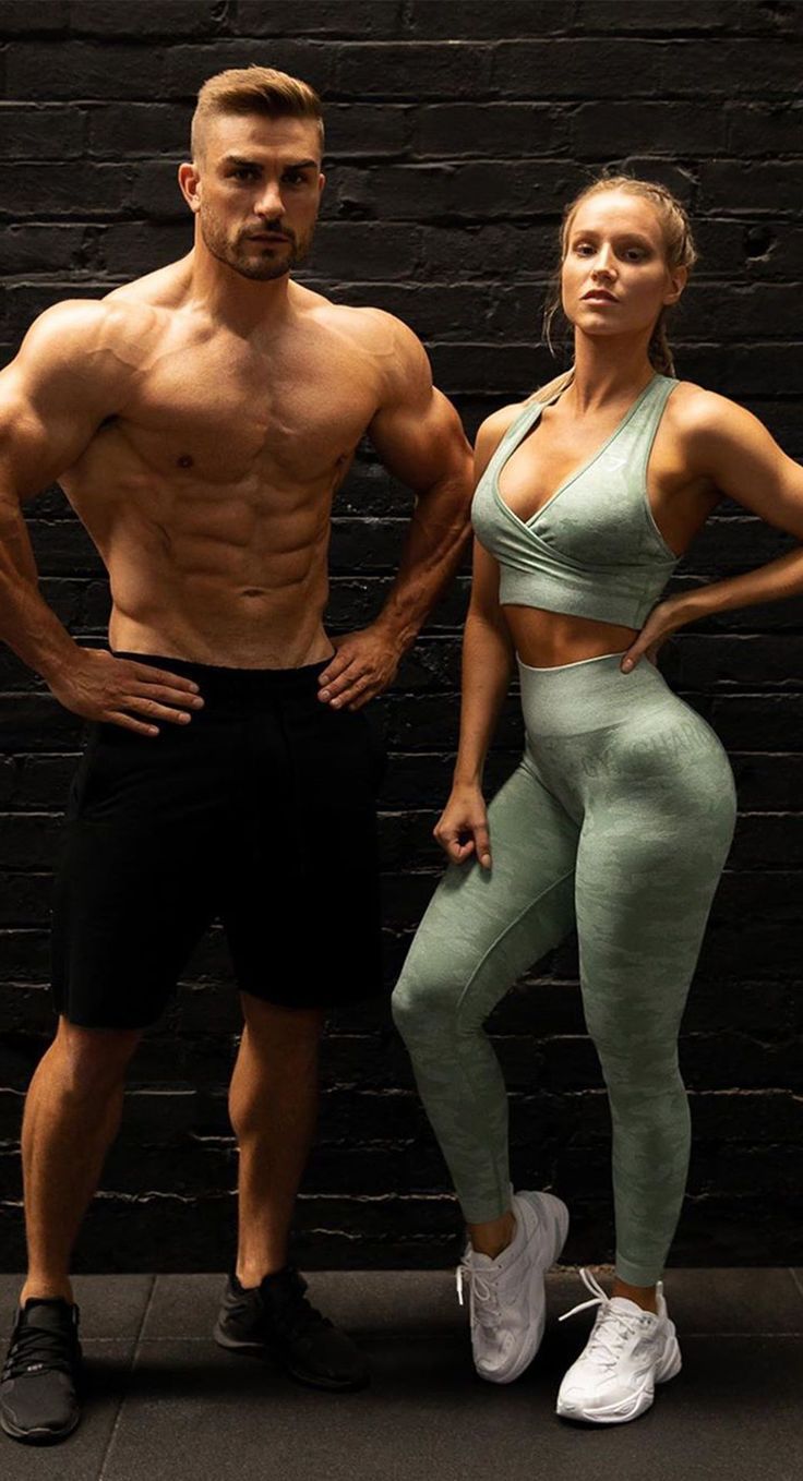 a man and woman standing next to each other in front of a black brick wall