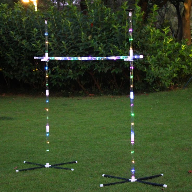 a cross made out of lights in the middle of a yard with grass and bushes behind it